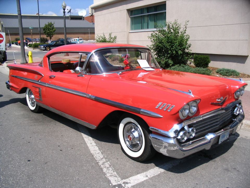 Red 1958 Chevrolet Impala coupe with chrome trim and whitewall tires parked on a street