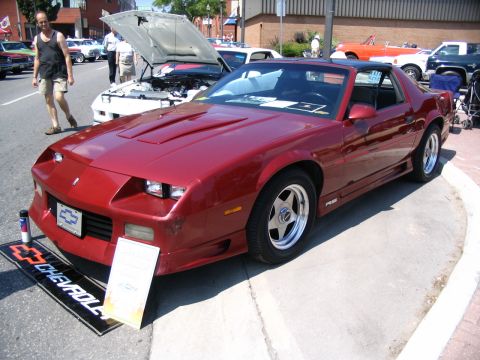 1993 Ford Taurus - A red 1980s Chevrolet Camaro IROC-Z is displayed at a car show, its distinctive body style and aftermarket wheels.