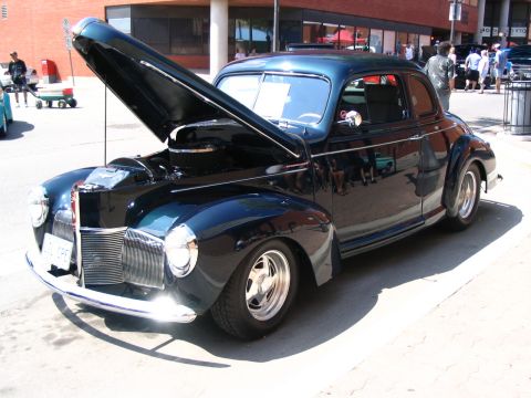 1993 Ford Taurus - A dark blue coupe from the 1940s is displayed with its hood open at a car show.