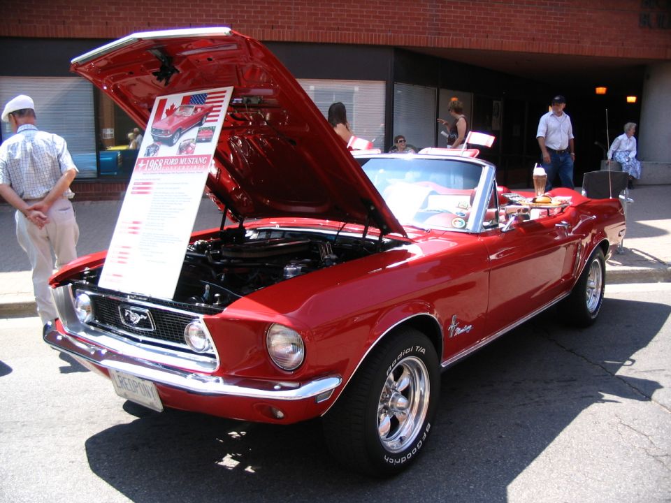 Red 1969 Ford Mustang convertible with hood open, showing a display board
