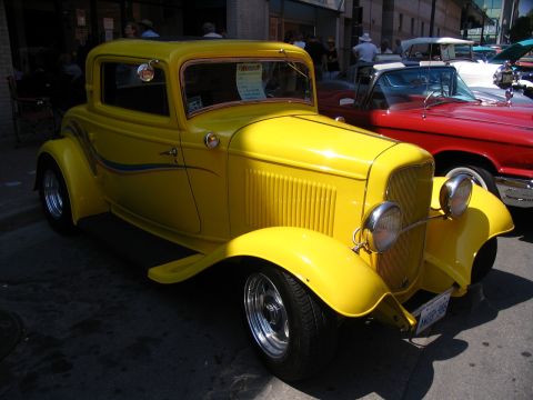 1993 Ford Taurus - A bright yellow hot rod coupe with a distinctive grille and pinstriping is displayed at a car show.
