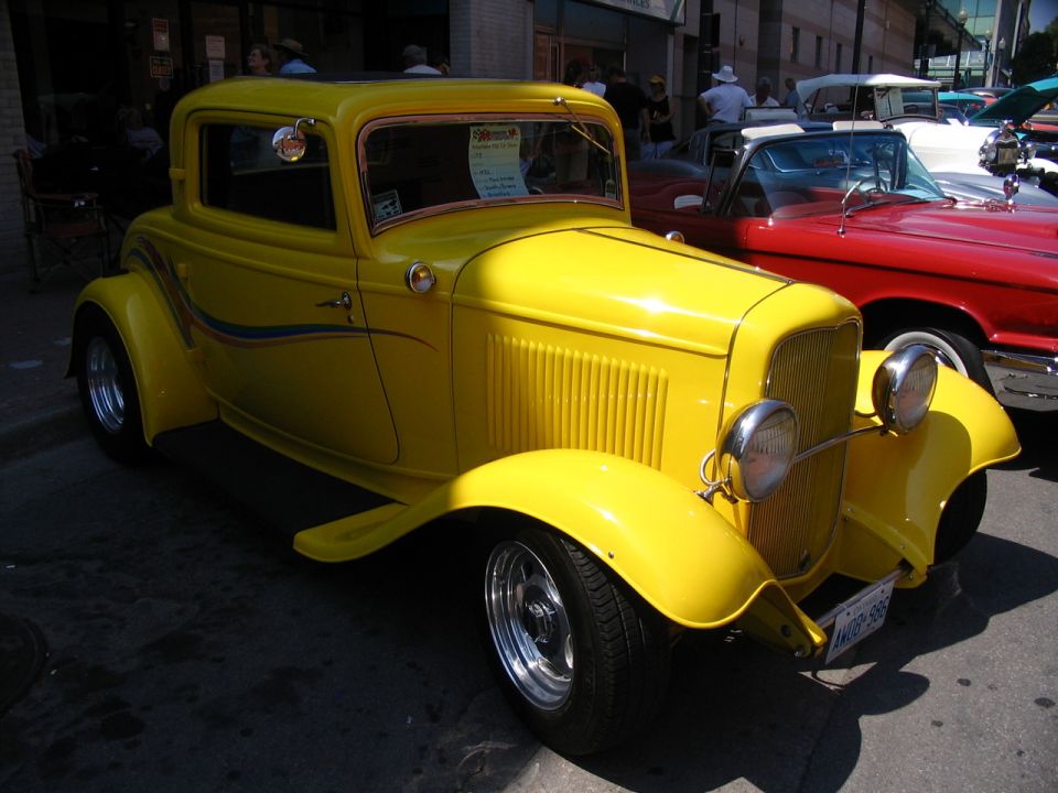 Yellow hot rod coupe with custom pinstriping, parked next to a red convertible