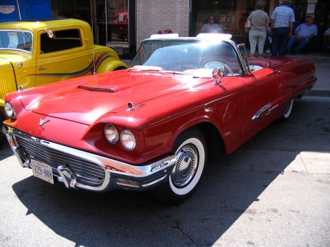 1993 Ford Taurus - A red 1958 Ford Thunderbird convertible is parked on a street next to a yellow classic car.