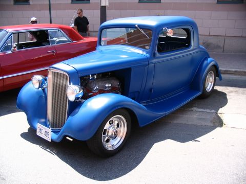 1993 Ford Taurus - A blue hot rod coupe is parked next to a red car at a car show.
