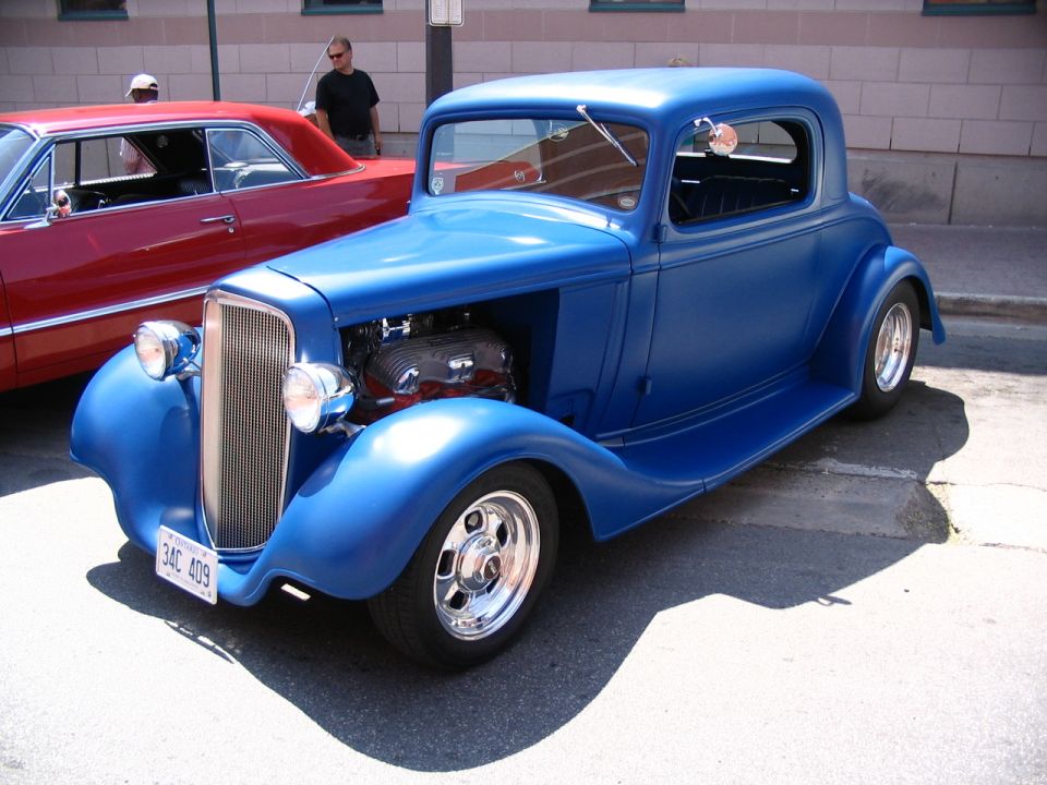 Blue hot rod coupe with exposed engine, parked next to a red car. License plate reads 34C 409