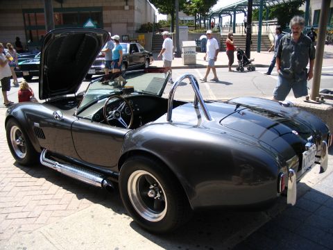 1993 Ford Taurus - A dark grey convertible sports car is displayed with its hood open at an outdoor event.