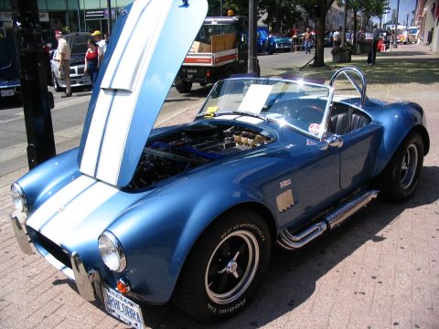 1993 Ford Taurus - A blue convertible sports car with its hood open is parked on a street, likely at a car show.