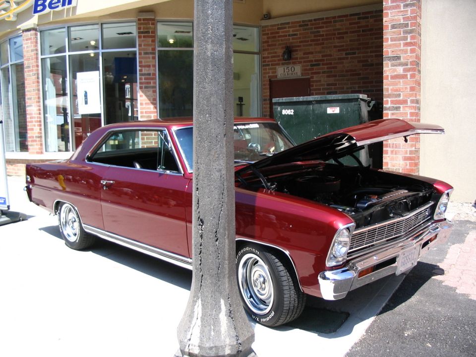 maroon coupe parked outside a building, hood is open showing the engine bay