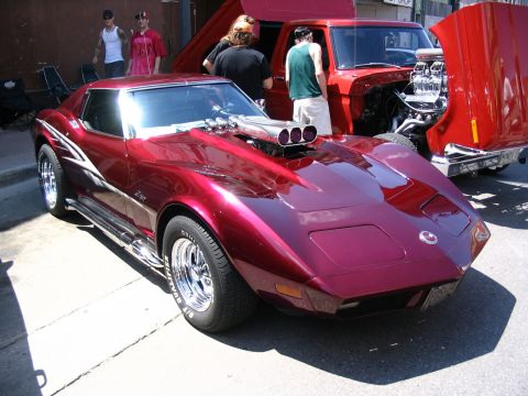 1993 Ford Taurus - Maroon Corvette Stingray with custom hood scoop and side pipes, seen at a car show with a red pickup truck.