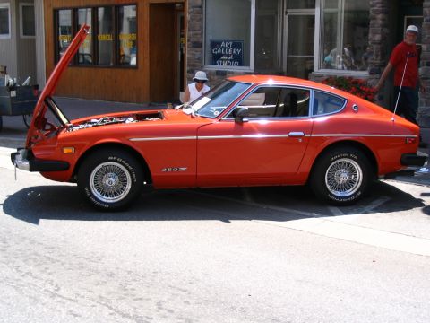 1993 Ford Taurus - Orange 1977 Datsun 280Z sports car displayed with its hood up at an outdoor event.