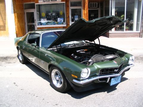 1993 Ford Taurus - Green 1970 Chevrolet Camaro SS with hood open, parked on street in front of building.