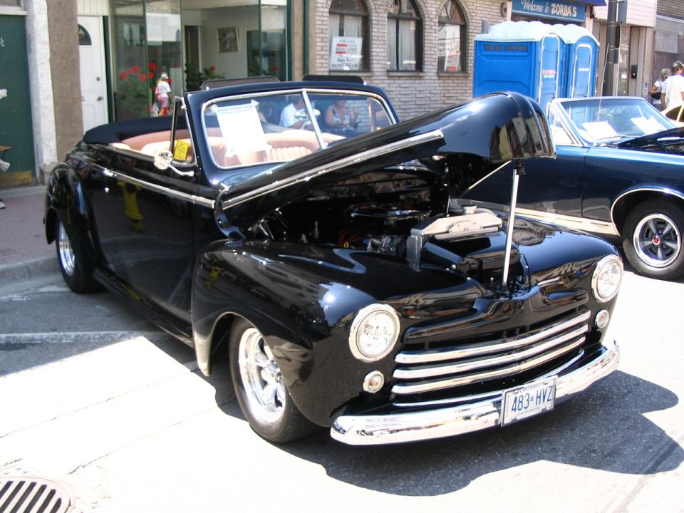 Black 1946 Ford convertible with hood open, parked next to a dark blue car