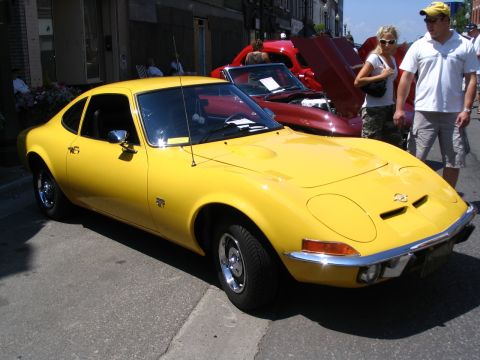 1993 Ford Taurus - A bright yellow Opel GT is displayed at an outdoor car show, with another car and onlookers in the background.