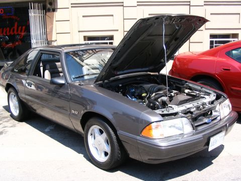 1993 Ford Taurus - Gray Ford Mustang with its hood open, revealing the engine, parked next to a red car.