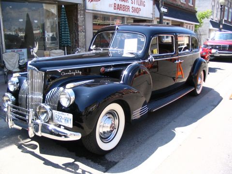 1993 Ford Taurus - A classic black Packard sedan is parked on a street in front of a barber shop, with another vehicle visible in the background.
