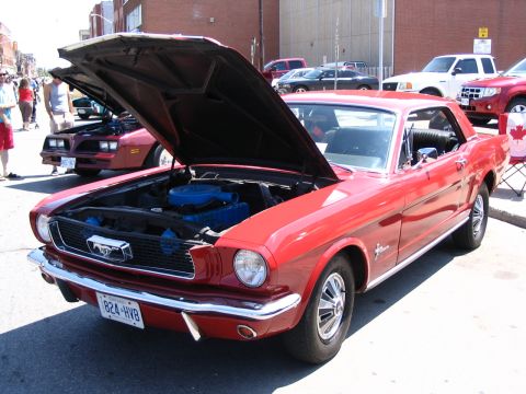 1993 Ford Taurus - Classic red Ford Mustang coupe with its hood open at a car show, parked next to another vehicle.