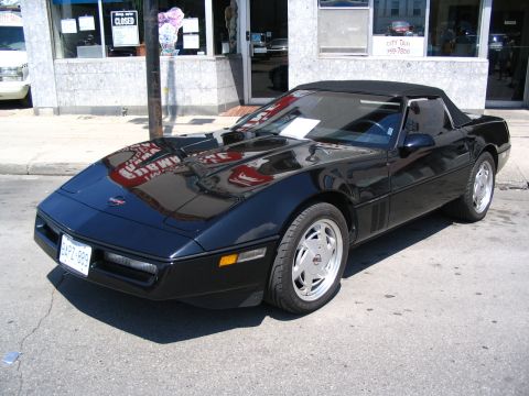 1993 Ford Taurus - This black convertible sports car is parked on a city street in front of a building.