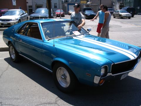 1993 Ford Taurus - A blue muscle car with white racing stripes is parked on a street, with people standing nearby.