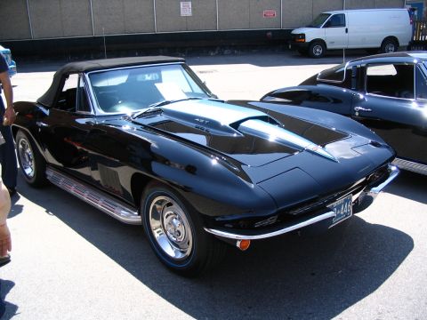 1993 Ford Taurus - Black convertible sports car parked next to another vehicle, with a white van in the background.