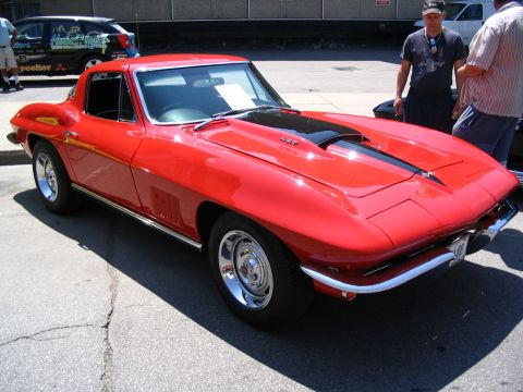 1993 Ford Taurus - A bright red Chevrolet Corvette Sting Ray is parked outside, with two men standing nearby.