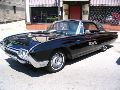 1993 Ford Taurus - A black 1963 Ford Thunderbird coupe is parked on a city street in front of a building with awnings.