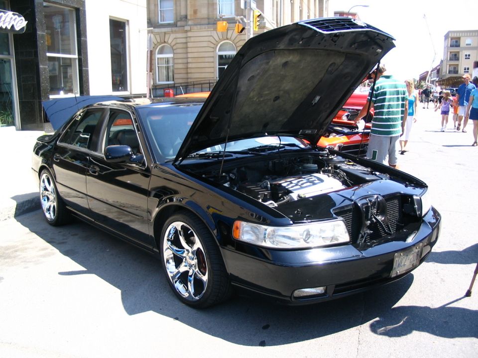 Black sedan with hood and trunk open, showing engine and interior. Chrome wheels visible