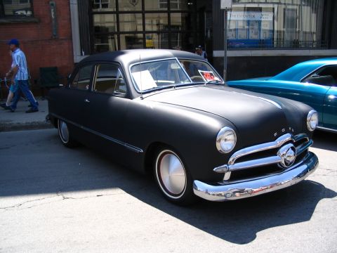 1993 Ford Taurus - A matte black 1949 Ford sedan is parked on a city street next to a blue car.
