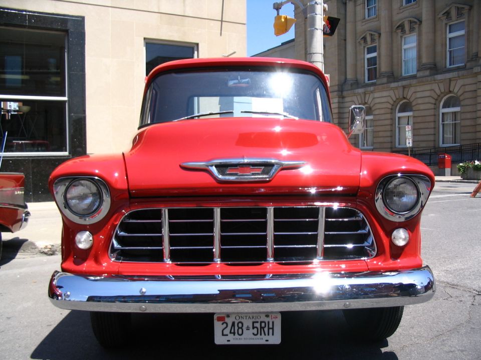 Red 1955 Chevrolet truck front view with chrome grille and bumper