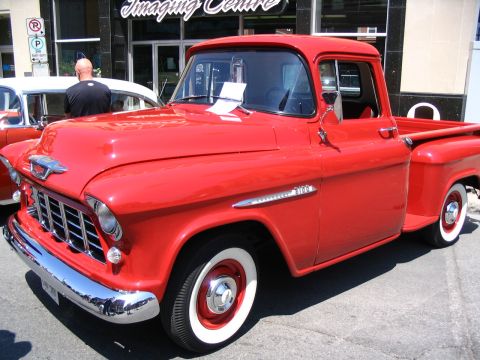 1993 Ford Taurus - A red 1955 Chevrolet pickup truck is parked next to another vehicle at an outdoor event.