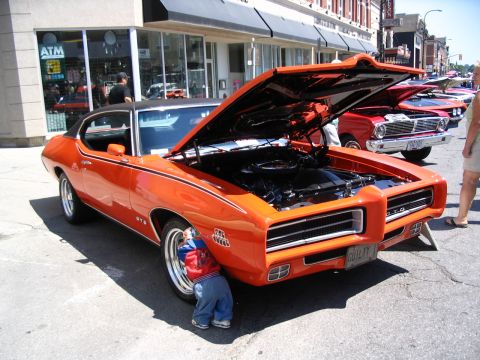 1993 Ford Taurus - A child peeks under the wheel of an orange 1969 Pontiac GTO at a car show.