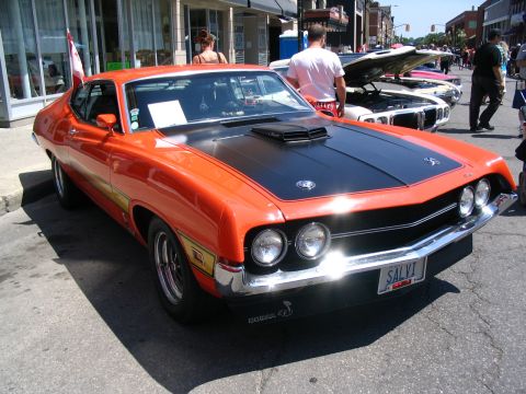 1993 Ford Taurus - A vintage orange Ford Torino GT is displayed at a car show with its hood open.
