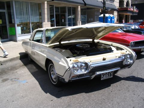 1993 Ford Taurus - A cream-colored 1963 Ford Thunderbird is displayed with its hood open at a car show, parked alongside other vehicles.