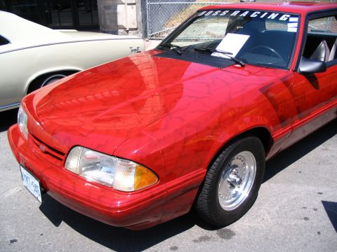 1993 Ford Taurus - A red 1993 Ford Mustang is parked next to another car, displaying racing decals.