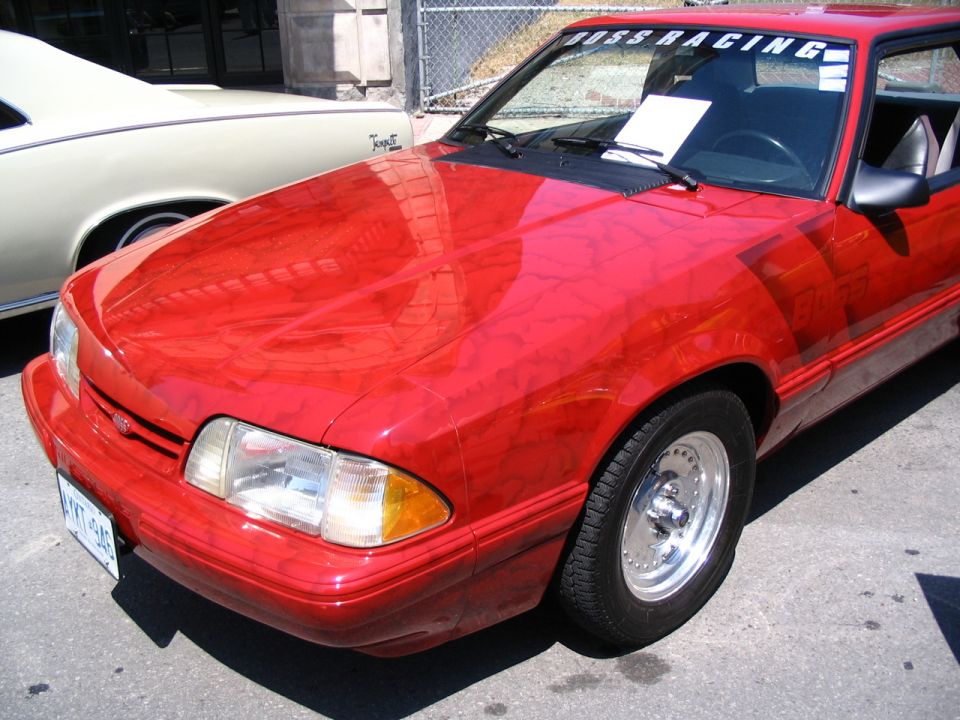 Red 1993 Ford Mustang with 'BOSS RACING' decal on windshield and chrome wheels