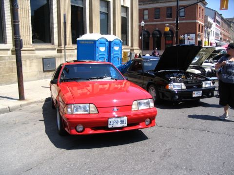 1993 Ford Taurus - Two Ford Mustangs are parked on a street, one red and one black with its hood open.