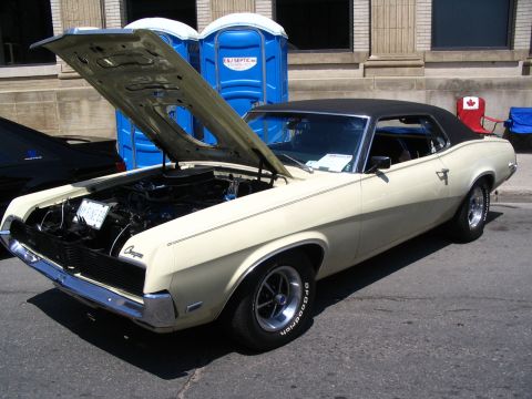 1993 Ford Taurus - A cream 1969 Mercury Cougar is displayed with its hood open, parked outdoors near portable restrooms.