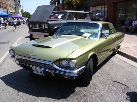 1993 Ford Taurus - A green 1965 Ford Thunderbird is parked on the street, with a black International Harvester Scout behind it at a car show.