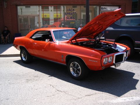1993 Ford Taurus - An orange 1969 Pontiac Firebird coupe is parked on a street with its hood open, next to a dark SUV.