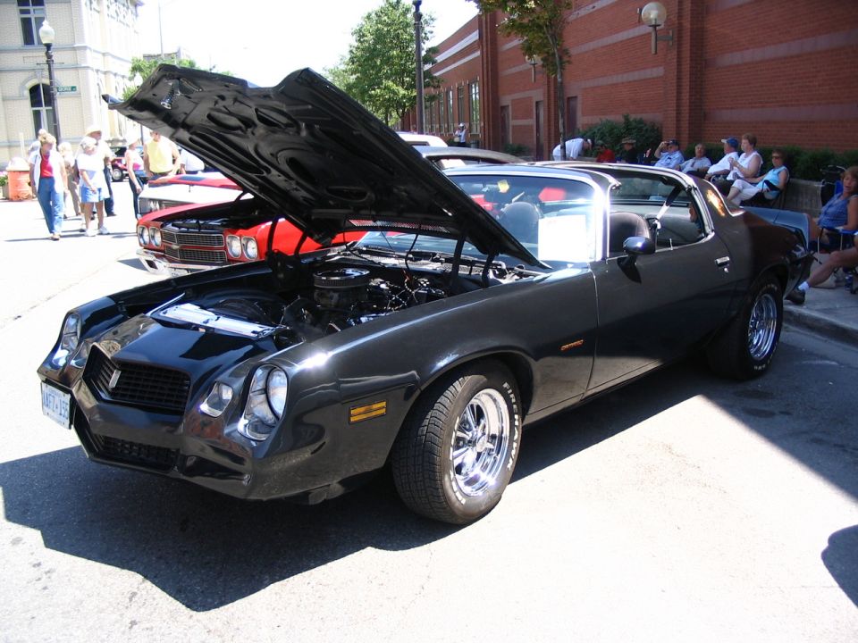 Black 1978 Chevrolet Camaro Z28 with hood open, parked on street next to red car