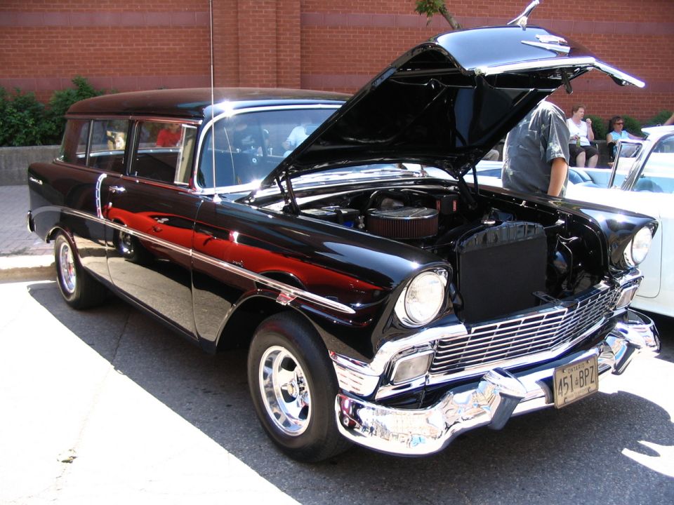 Black 1956 station wagon, hood open, showing engine. Chrome grille and bumper