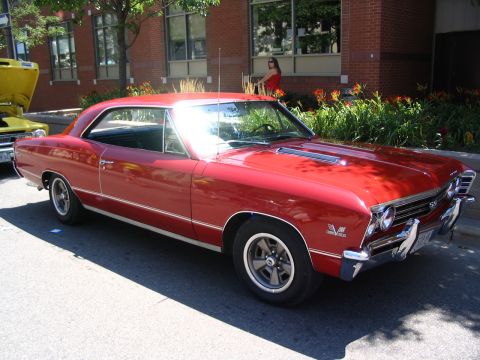 1993 Ford Taurus - A red 1967 Chevrolet Chevelle SS coupe is parked at a car show, with another vehicle visible to its left.