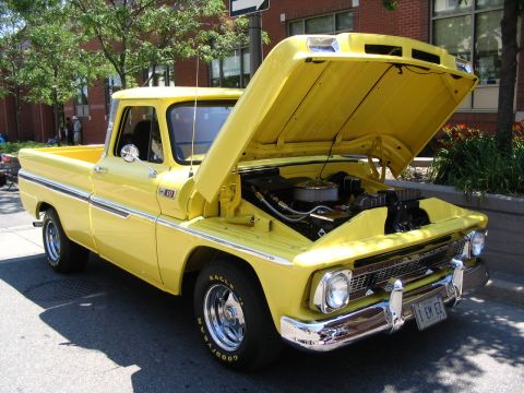 1993 Ford Taurus - Yellow 1966 Chevrolet C10 pickup truck displayed with its hood open at a car show.