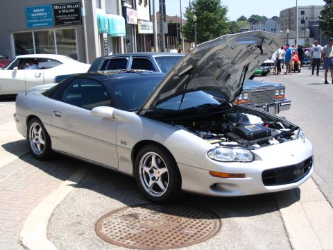 1993 Ford Taurus - A silver Chevrolet Camaro SS is parked on the street with its hood open, showing the engine bay.