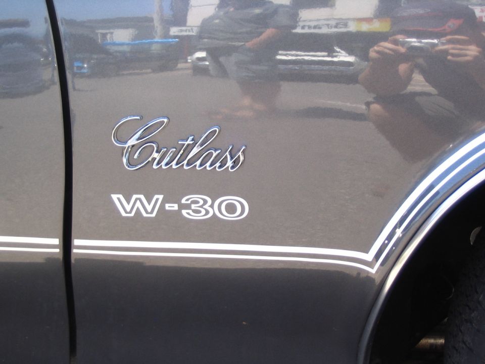 Side view of an Oldsmobile Cutlass W-30 with chrome badging and white racing stripes
