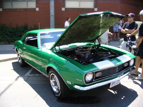 1993 Ford Taurus - A green 1969 Chevrolet Camaro is displayed with its hood open at a car show.