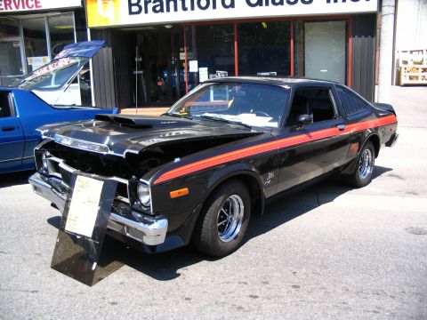 1993 Ford Taurus - A black 1976 Dodge Aspen with orange racing stripes is displayed with its hood open outside a business.