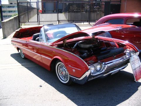 1993 Ford Taurus - A red 1962 Ford Thunderbird convertible is displayed with its hood open, parked next to another red vehicle.