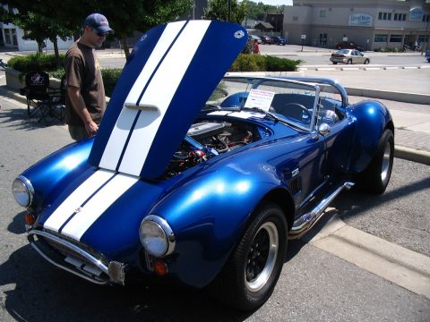 1993 Ford Taurus - A blue convertible sports car with white racing stripes is displayed with its hood open at an outdoor car show.