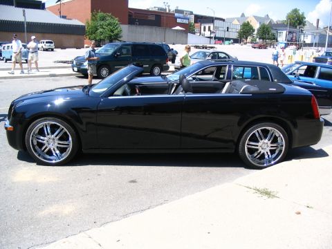 1993 Ford Taurus - A black convertible sedan with custom chrome wheels is parked on a city street.