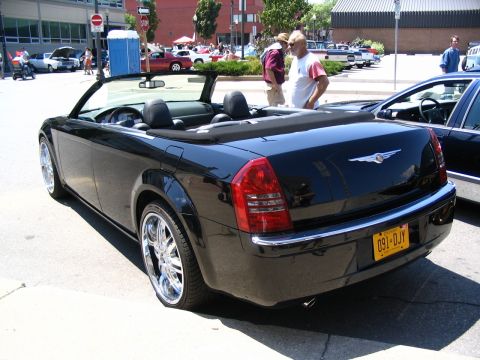 1993 Ford Taurus - A black convertible is parked on a street with other vehicles and people around.